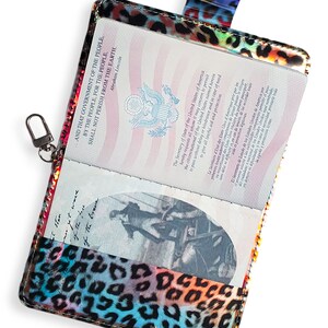 K&ouml;nnte beinhalten: Ein Reisepass-Etui mit Leopardenmuster. Das Etui ist aus gl&auml;nzendem, irisierendem Material mit einem Regenbogen an Farben gefertigt. Das Etui hat einen Rei&szlig;verschluss und eine kleine Schlaufe zum Anbringen eines Schl&uuml;sselanh&auml;ngers.