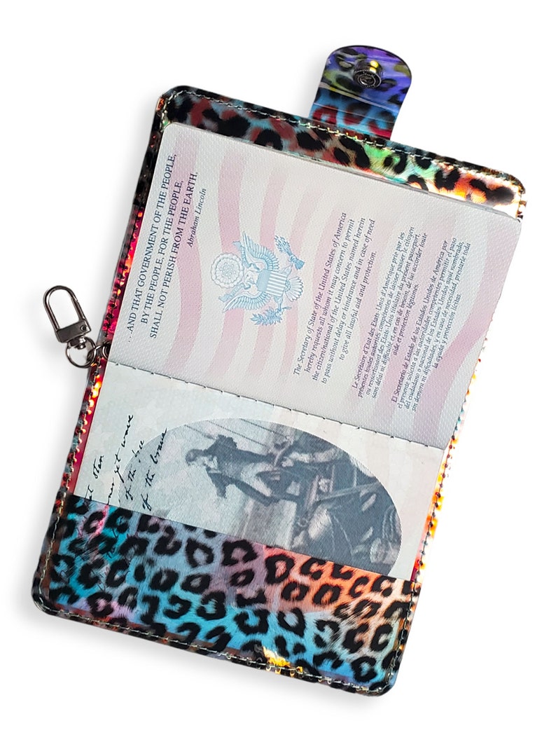 K&ouml;nnte beinhalten: Ein Reisepass-Etui mit Leopardenmuster. Das Etui ist aus gl&auml;nzendem, irisierendem Material mit einem Regenbogen an Farben gefertigt. Das Etui hat einen Rei&szlig;verschluss und eine kleine Schlaufe zum Anbringen eines Schl&uuml;sselanh&auml;ngers.