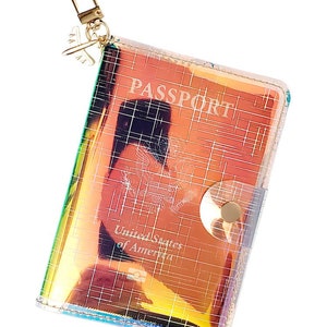 Funda para pasaporte holográfica con detalles de líneas láser. Funda para pasaporte hecha de vinilo holográfico. Funda para pasaporte con dije de avión.