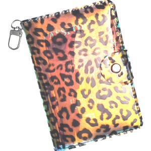 K&ouml;nnte beinhalten: Ein transparenter Reisepass-Etui mit Leopardenmuster. Das Etui hat einen Rei&szlig;verschluss und einen kleinen Schl&uuml;sselring.