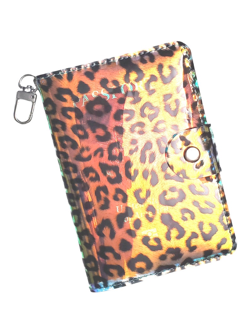 K&ouml;nnte beinhalten: Ein transparenter Reisepass-Etui mit Leopardenmuster. Das Etui hat einen Rei&szlig;verschluss und einen kleinen Schl&uuml;sselring.