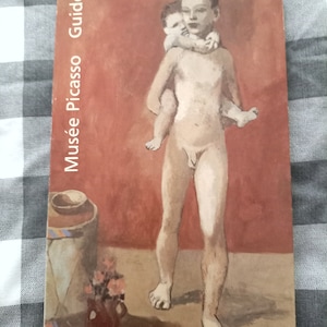 Puede incluir: Una portada de libro con una pintura de dos figuras desnudas. Las figuras son una mujer joven que sostiene a un niño más pequeño. El fondo es de color rojo-naranja. El título del libro es "Musée Picasso Guide".