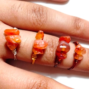 May include: Four handmade rings with orange carnelian stones. Each ring features a different wire color: silver, gold, copper, and dark copper. The carnelian stones are stacked on the wire, creating a unique and natural look.