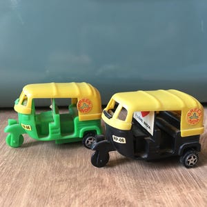 Könnte beinhalten: Zwei Spielzeug-Autorikschas, eine grüne und gelbe, die andere schwarz und gelb. Auf der grünen Rikschas steht "Green India". Auf der schwarzen Rikscha steht "I Love India" auf einer kleinen Flagge.