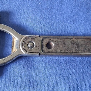 May include: A vintage silver-toned metal cork puller and bottle opener with a T-shaped handle. The rectangular handle features the embossed text QUICK AND EASY CORK PULLER AND BOTTLE OPENER. The metal surface shows signs of wear and oxidation.