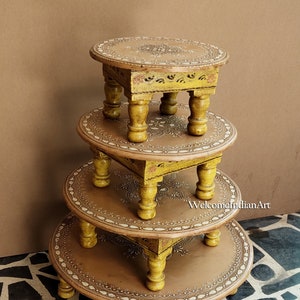 May include: Set of four round wooden stools with intricate hand-painted designs in yellow and brown. The stools are stacked on top of each other, with the smallest on top. The stools have a decorative border and four legs.