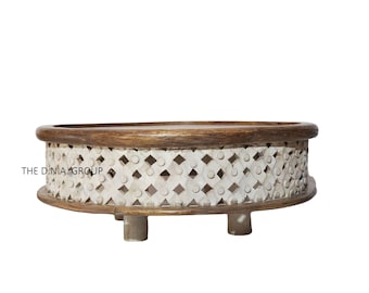 May include: A round wooden coffee table with a white painted base and intricate carved details. The table has a brown top and four short legs.