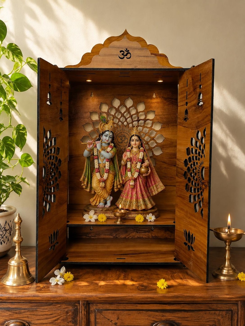 K&ouml;nnte beinhalten: Ein h&ouml;lzerner Heimtempel mit einem Om-Symbol an der Oberseite, filigranen lasergeschnittenen Blumenmustern an den T&uuml;ren und Innenbeleuchtung. Im Inneren stehen Statuen von Krishna mit Fl&ouml;te und Radha auf einem Sockel, erg&auml;nzt durch eine kleine &Ouml;llampe.