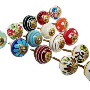 May include: A collection of 15 colorful ceramic cabinet knobs with gold accents. Each knob features a unique design with various patterns and colors, including green, red, blue, white, and black.
