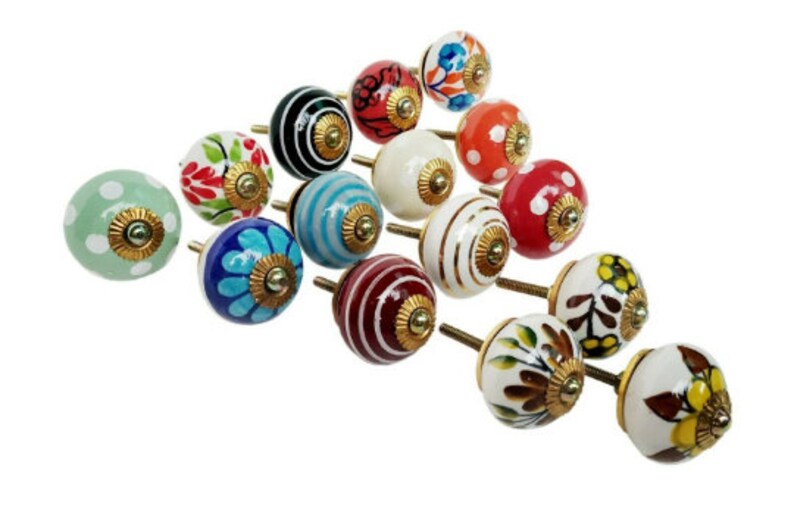 May include: A collection of 15 colorful ceramic cabinet knobs with gold accents. Each knob features a unique design with various patterns and colors, including green, red, blue, white, and black.