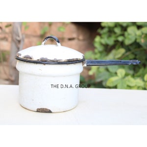 May include: White enamel saucepan with a black handle and a black rim. The saucepan has a lid with a black handle. The saucepan is slightly chipped and shows signs of wear.