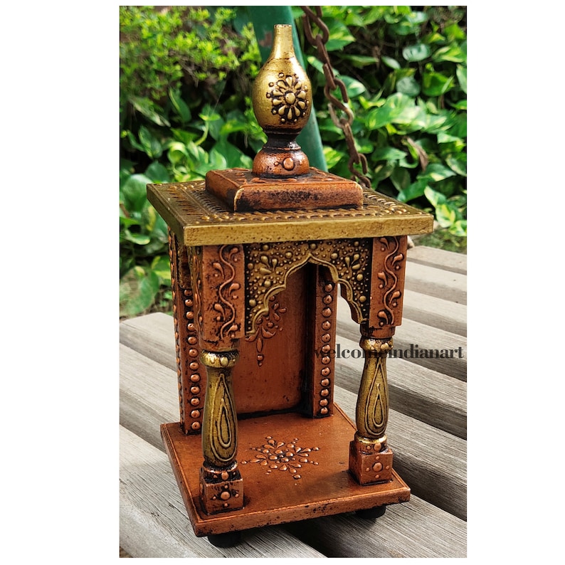 Puede incluir: Un peque&ntilde;o templo de madera tallado intrincadamente con un acabado dorado y cobre. El templo tiene una parte superior decorativa con un dise&ntilde;o floral y una peque&ntilde;a c&uacute;pula redondeada. El templo est&aacute; decorado con tallas y detalles intrincados, incluidos patrones florales y un peque&ntilde;o arco.