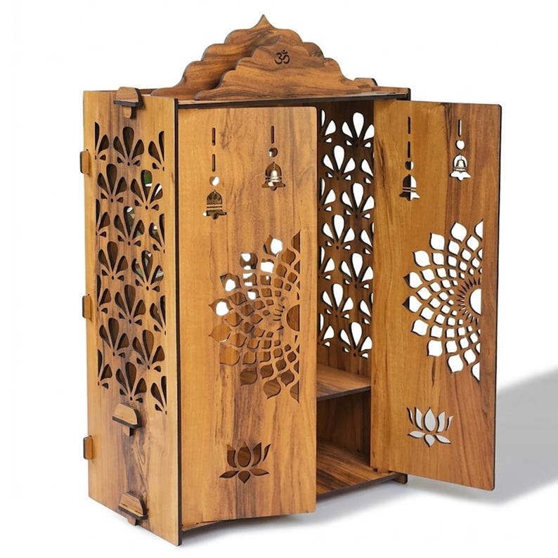 K&ouml;nnte beinhalten: Ein h&ouml;lzerner Haustempel-Schrank mit komplizierten, lasergeschnittenen Blumen- und Lotusmustern auf den T&uuml;ren und Seitenteilen. Die Struktur umfasst ein spitzes Dach mit einem Om-Symbol, zwei offene T&uuml;ren, Innenregale und kleine Glockenmotive.