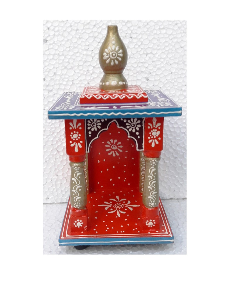 Puede incluir: Un peque&ntilde;o templo de madera rojo con un remate dorado en la parte superior. El templo tiene detalles pintados en blanco y acentos azules y morados. Est&aacute; decorado con motivos florales.