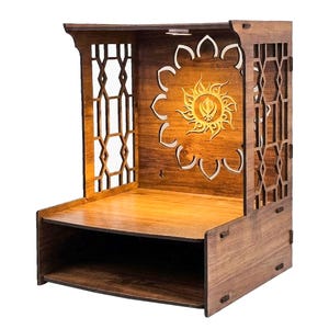 May include: A brown wooden home temple featuring a laser-cut lattice design on the side panels and a central back panel with a cutout of a sunburst motif surrounding a Khanda symbol. The structure includes a flat shelf and a lower storage compartment.