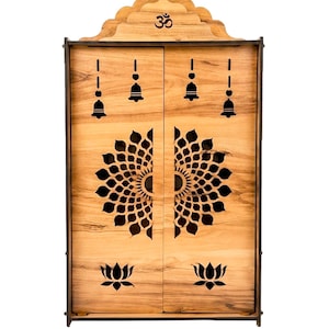 K&ouml;nnte beinhalten: Ein hellbrauner, wandmontierter Schrein aus Holz mit zwei T&uuml;ren und aufwendigen Laserschnitt-Designs. Oben ist ein Om-Symbol zu sehen, w&auml;hrend die T&uuml;ren Ausschnitte von h&auml;ngenden Glocken, einem gro&szlig;en kreisf&ouml;rmigen Blumen-Mandala-Muster und Lotusblumen zeigen.