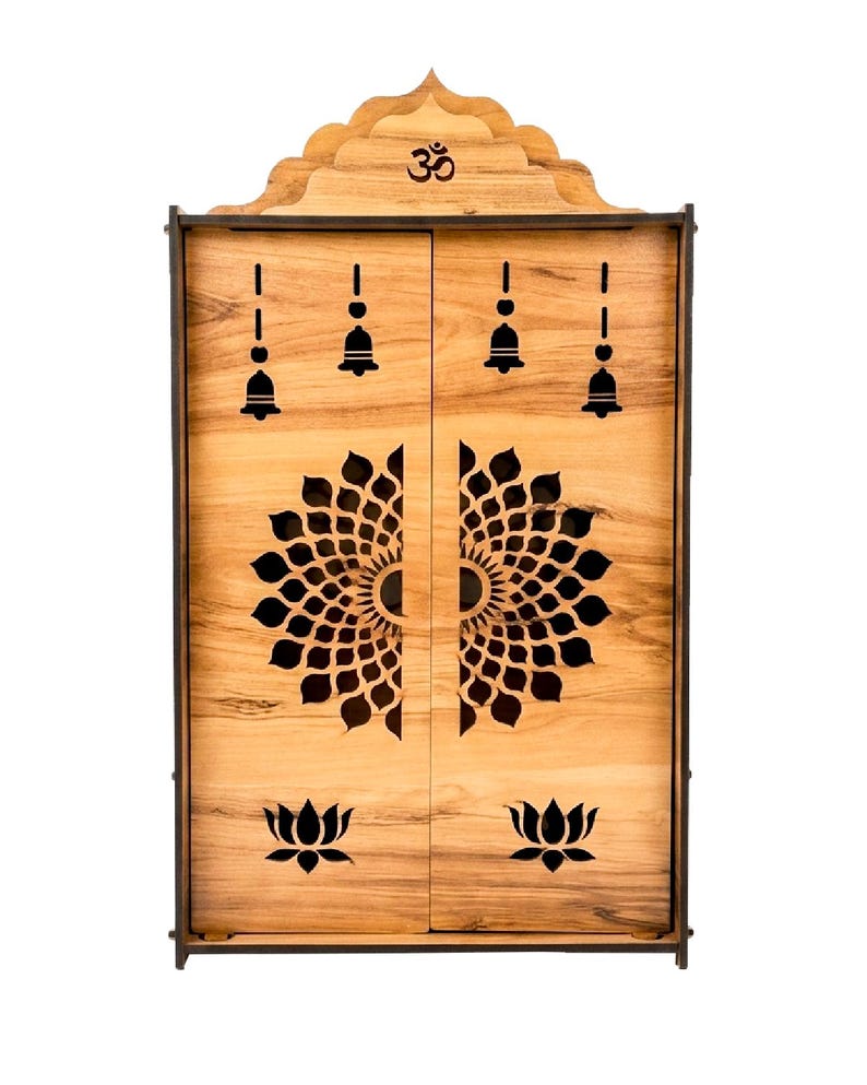 K&ouml;nnte beinhalten: Ein hellbrauner, wandmontierter Schrein aus Holz mit zwei T&uuml;ren und aufwendigen Laserschnitt-Designs. Oben ist ein Om-Symbol zu sehen, w&auml;hrend die T&uuml;ren Ausschnitte von h&auml;ngenden Glocken, einem gro&szlig;en kreisf&ouml;rmigen Blumen-Mandala-Muster und Lotusblumen zeigen.