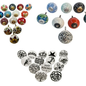 May include: Assortment of ceramic cabinet knobs with various designs. Some knobs feature floral patterns in shades of blue, red, and yellow. Others have a white background with black designs, including a crown, a star, and the word "HER".