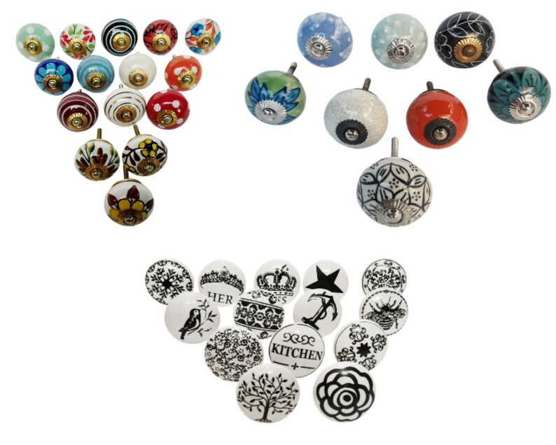 May include: Assortment of ceramic cabinet knobs with various designs. Some knobs feature floral patterns in shades of blue, red, and yellow. Others have a white background with black designs, including a crown, a star, and the word "HER".