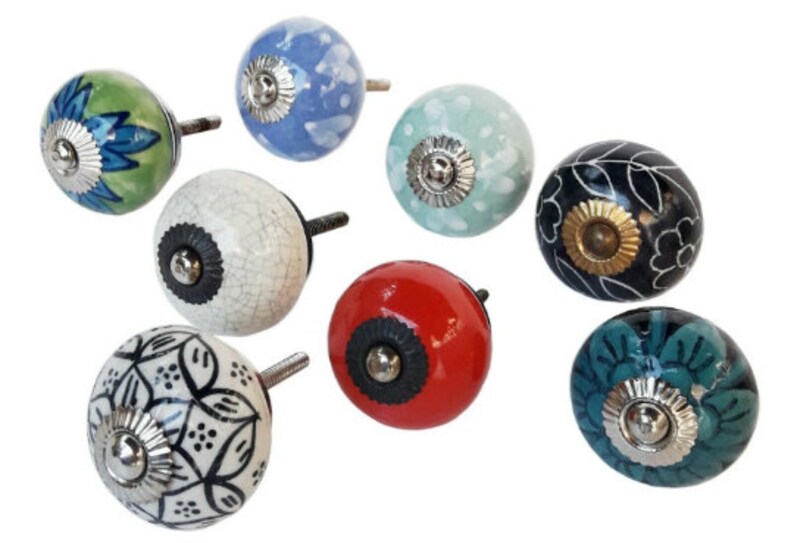 May include: Assortment of eight ceramic cabinet knobs with various floral and geometric patterns. The knobs are in shades of blue, green, white, black, red, and teal. Each knob has a silver metal base.