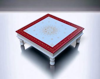 May include: A square, low-profile table with four short, turned legs. The tabletop features a light blue centre with a gold mandala-style pattern, surrounded by a wide, deep red border decorated with intricate gold filigree and floral motifs.