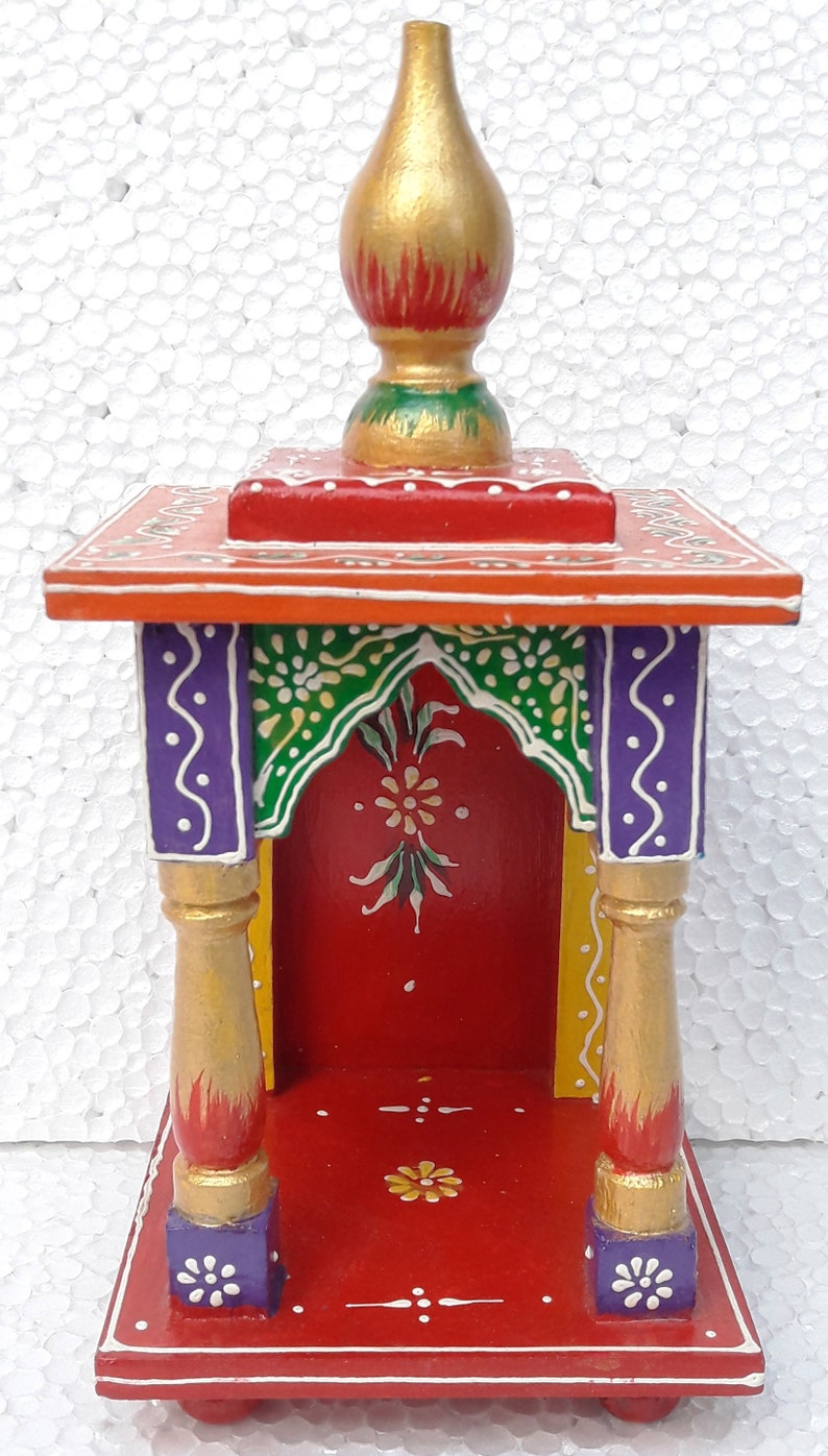 Puede incluir: Un peque&ntilde;o templo de madera pintado a mano con una base roja, acentos verdes y morados y un remate pintado en oro. El templo tiene una peque&ntilde;a abertura en la parte delantera para colocar una estatua u otros objetos religiosos.