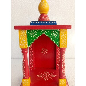 Puede incluir: Un peque&ntilde;o templo de madera pintado a mano con una base roja, acentos verdes y amarillos y un remate amarillo. El templo tiene una peque&ntilde;a abertura en la parte delantera y est&aacute; decorado con dise&ntilde;os florales blancos.