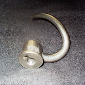 Puede incluir: Gancho para masa de metal plateado para una batidora de pie. El gancho tiene una forma curva y una base redonda con un agujero en el centro.