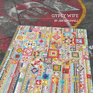 Puede incluir: Una colcha colorida con una variedad de patrones y colores, incluyendo rojo, amarillo, azul, verde y blanco. La colcha est&aacute; hecha de cuadrados y rect&aacute;ngulos, y tiene un borde azul. La colcha se titula "Gypsy Wife" por Jen Kingwell.