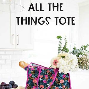 May include: A floral tote bag with pink handles and a dark blue background. The bag is filled with a baguette and flowers. The text "ALL THE THINGS TOTE" is displayed above the bag. The text "KNOT + THREAD design" is displayed below the bag.