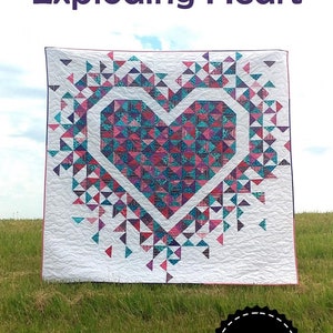 May include: A quilt featuring a large pink and blue heart design, surrounded by smaller triangles. The quilt is called "Exploding Heart" and is made by Slice of Pi Quilts.