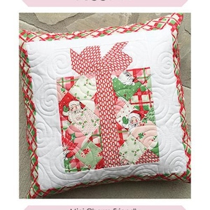 Op de afbeelding: Een gewatteerd kussen met een kerstcadeau-ontwerp. Het kussen heeft een witte achtergrond en een rood-groene patroonrand. Het centrale ontwerp is een geschenkdoos met een rode strik en afbeeldingen van de kerstman. Afmeting is 45,7 cm x 45,7 cm. De tekst "Pretty Present Pillow" staat bovenaan.