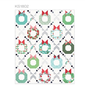 May include: A quilt pattern titled "Merry & Bright" featuring Christmas wreaths with red bows. The wreaths are in shades of green and blue, set against a white background with geometric accents. The pattern is by Kate Spain.