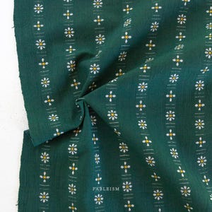 May include: Dark green fabric with a repeating pattern of white and yellow floral designs arranged in vertical stripes. The fabric is folded, showing texture and the word "FABLEISM" in white.