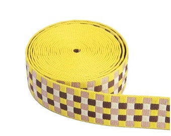 May include: A yellow and brown checkered webbing strap. The strap is rolled up and the checkered pattern is visible on the outside of the roll.