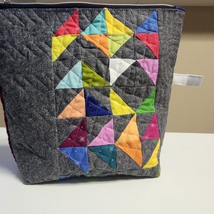 May include: A gray quilted zippered pouch with a colorful patchwork design of triangles in various colors, including red, yellow, green, blue, pink, and orange.