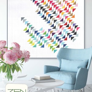 May include: A framed colorful geometric quilt pattern with a white background. The quilt is titled "SKY" in red text. The quilt is displayed on a white wall above a blue armchair and a white coffee table.
