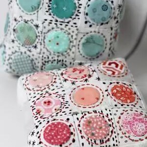 May include: Two handmade fabric boxes with a patchwork design. The boxes are white with colorful polka dots in shades of pink, coral, and teal. The boxes are square and have a quilted appearance.