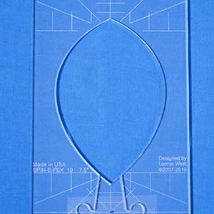 May include: A clear plastic template for sewing, labeled "SPIN-E-FEX 10 7.5" and "SFEX10 7.5". The template features a large leaf shape with a pointed tip and a curved bottom. The template is designed by Leonie West and is copyright 2007-2019.