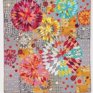 May include: A colorful quilt with a gray background and large, circular, starburst-like designs in shades of red, yellow, blue, and orange. The quilt features various patterned fabrics and red polka dots. The text "AARDVARK QUILTS" is at the bottom.