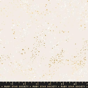 May include: Cream-colored fabric with a speckled pattern of gold and white dots. The fabric has a subtle texture and a soft, neutral background. The bottom of the fabric has a black ruler with the text "RUBY STAR SOCIETY".