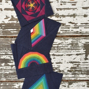 May include: Four fabric squares with geometric designs. The top square is a dark red with a spiral design. The second square is dark blue with a rainbow diamond shape. The third square is dark blue with a rainbow arch. The bottom square is dark blue with a green triangle.