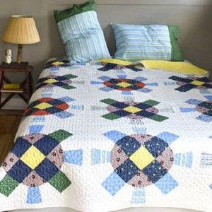 Pode incluir: Uma colcha de retalhos com fundo branco e um padrão repetitivo de círculos e quadrados coloridos. A colcha é feita com uma variedade de tecidos, incluindo azul, verde, amarelo e vermelho.