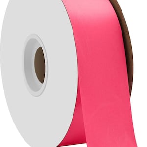 Puede incluir: Una bobina de cinta de satén rosa brillante. La cinta está enrollada alrededor de una bobina de cartón blanco.