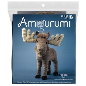 May include: A crochet kit featuring a brown moose with large antlers. The kit is labeled "Amigurumi" and includes the text "Moose Elan intermediate". The packaging is in a clear plastic bag.