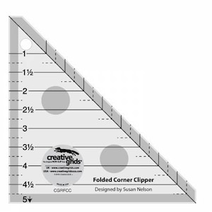 Könnte beinhalten: Ein durchsichtiges Lineal aus Kunststoff mit Markierungen in Zoll, beschriftet mit "Folded Corner Clipper" und "Designed by Susan Nelson". Das Lineal hat die Form eines rechtwinkligen Dreiecks mit einer Seite von 5 Zoll und einer Hypotenuse von 5 Zoll.