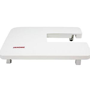 Peut inclure: Table d'extension blanche pour machine à coudre avec le nom de marque "JANOME" en rouge. La table est de forme rectangulaire avec une découpe sur un côté et est soutenue par quatre pieds carrés.
