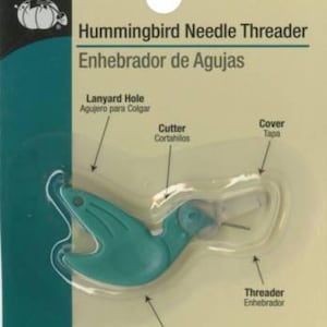 May include: A green plastic hummingbird needle threader with a cutter, a cover, a lanyard hole, and a finger grip. The text "Hummingbird Needle Threader" and "Enhebrador de Agujas" is printed on the packaging.