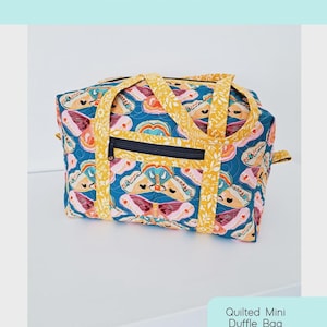 Könnte beinhalten: Eine gesteppte Mini-Duffel-Tasche mit einem leuchtend blauen Hintergrund und einem farbenfrohen Muster. Die Tasche hat einen schwarzen Reißverschluss und gelbe Griffe und Verzierungen. Der Text "Holland Duffle" wird oben angezeigt.