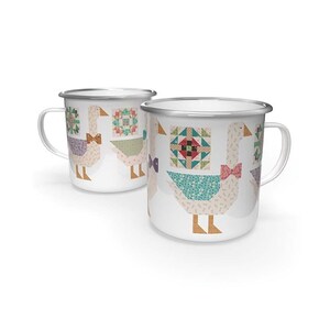 Könnte beinhalten: Zwei weiße Emaille-Tassen mit silbernen Rändern. Jede Tasse zeigt ein Gänsemotiv mit Fliege und Patchwork-Mustern in verschiedenen Farben. Die Tassen stehen vor einem weißen Hintergrund.
